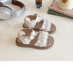 Dettaglio di sandali bianchi da bambina con fiori in pizzo e perle su fondo crema