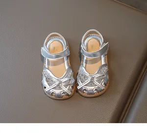 Detail of silver girls sandals with lace trim, shiny finish, and bow on leather background
