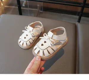 Nahaufnahme weißer Kindersandalen mit Schleifen-Detail und Herz-Lochmuster-Design