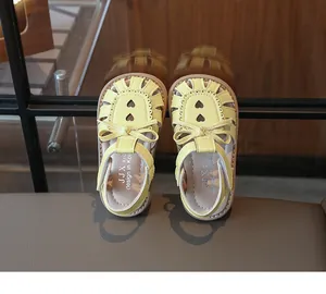 Detailansicht gelber Kindersandalen mit Schleifen-Deko und Herz-Ausschnittmuster