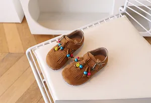 Detail van bruine suède loafers voor meisjes met etnische kwastjes en kleurrijke kralen