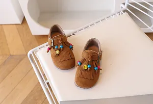 Detail van bruine suède meisjesschoenen met gekleurde kralen, kwastjes en gele smiley bedel