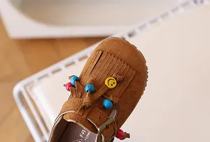 Detail van bruine leren meisjesschoenen met franjes, kralen en een gele smiley-bedeltje