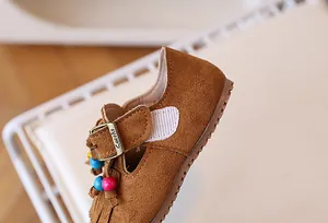 Detail van bruine suède kinderschoen met metalen gesp, kleurrijke kralen en franje decor