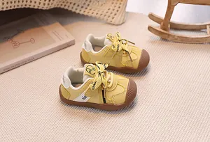 Detail view of yellow baby sneakers with anti-slip rubber soles on a soft home rug