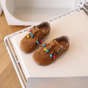 Bruine suède loafers voor meisjes met kwastjes en gekleurde kralen op een stoel