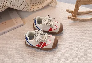 Detailed view of cream toddler shoes featuring red and blue stripes and gum rubber toes