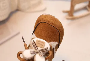 Detailed close-up of brown suede baby snow boots with plaid bow and fur trim