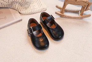 Top view of girls black Mary Jane leather shoes with silver buckle on a beige carpet