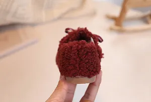 Detail of plush faux fur texture and bow decoration on baby winter shoes in burgundy