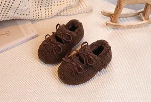 Detailed close-up of brown plush baby shoes with double leather bows on soft mat