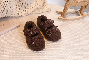 Detail view of brown plush baby shoes with patent leather bows on a cozy beige rug