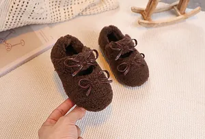 Detail of warm brown plush toddler shoes with decorative bow knots on a cozy beige mat