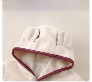 Détail de capuche bébé avec oreilles rondes et liseré bordeaux sur tricot crème doux
