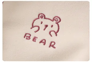 Détail de la broderie ours rose et texte BEAR sur le tricot crème pour bébé