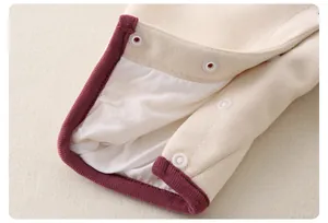 Détail d'une barboteuse en tricot pour bébé avec boutons-pression et bordure bordeaux