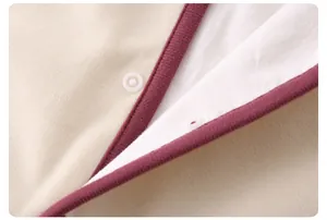 Détail d'une grenouillère bébé avec tricot beige, bordure rouge et bouton-pression blanc