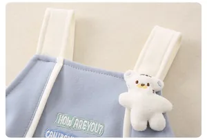 Dettaglio tutina neonato in maglia blu con ciondolo a forma di orso e ricamo raffinato