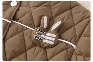 Detail der braunen Steppjacke mit süßer Kaninchenstickerei und weißen Knöpfen