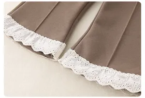 Detail of coffee brown pants showing delicate white lace trim and floral embroidery