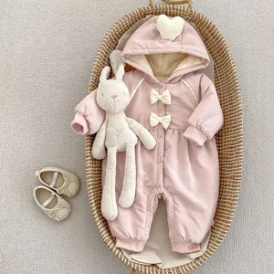 Detail eines rosa Baby-Overalls mit weißen Schleifen und Plüschhasen im Weidenkorb