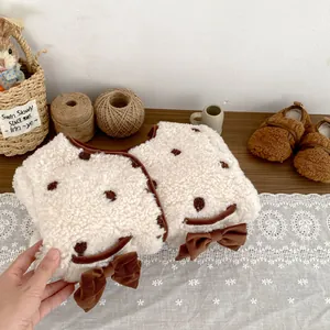 Dettaglio di un bavaglino in peluche per neonati con faccina e fiocco in velluto morbido