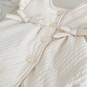 Detailed view of textured cream baby vest fabric with round buttons and bow accents