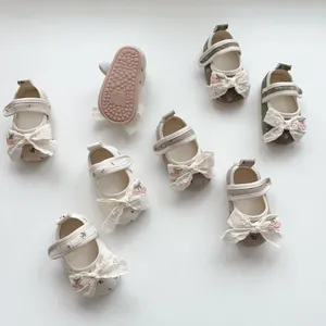 Detail of floral baby Mary Janes with lace bows and non-slip rubber soles with logo