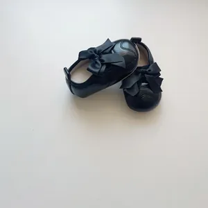 Détail de chaussures bébé en cuir noir avec grand nœud en satin et semelle antidérapante