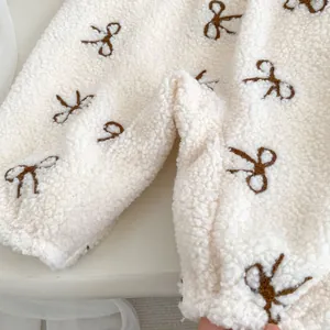 Detailed close-up of cream fleece baby bodysuit with brown bow embroidery patterns