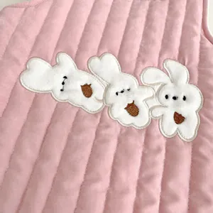 Close-up of pink quilted fabric with three white rabbit embroidery patches for baby bodysuit