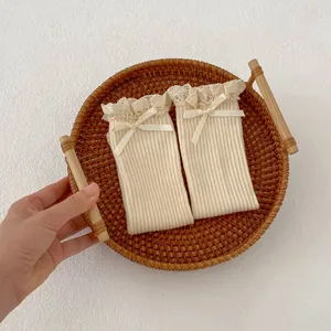 Detailed shot of beige cotton baby socks with lace ruffles and ribbon bows in a basket