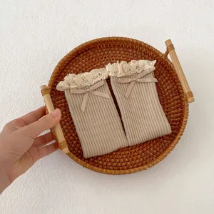 Close-up of beige ribbed knit baby socks with lace trim and delicate bow detail