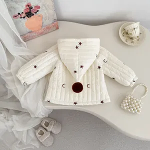 Detail der cremefarbenen Baby-Kapuzenjacke mit Stern-Mond-Print und Pelzbommel