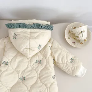 Close-up of cream quilted baby hooded romper with floral embroidery and ruffle trim