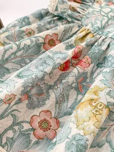 Makroaufnahme von grünem Blumenstoff mit Spitzenbesatz und Plissee-Details für Babykleidung