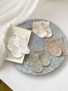 Mesh breathable baby socks in white, cream, and earth tones arranged in a rustic metal tray