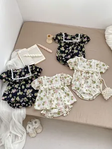 Flat lay of floral baby bodysuits with ruffle collars and lace details in a cozy setting