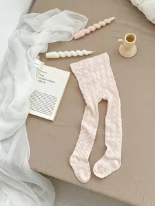 Close-up of baby girl pink hollow knit leggings with a delicate white bow detail