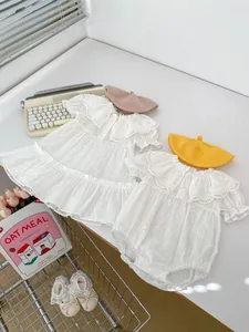 Flachbild von weißem Baby-Spitzenkleid und Strampler-Set mit Strickmützen und Schuhen