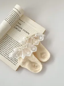 Detailed view of beige cotton baby socks featuring white lace trim and floral embroidery