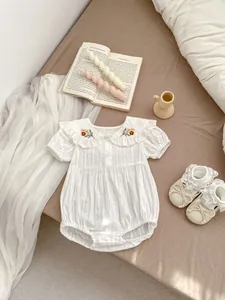 Close-up of floral embroidery on a white baby romper with a delicate doll collar