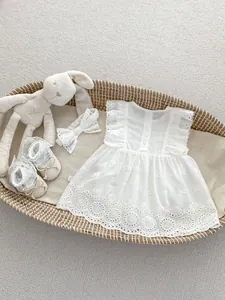 Detail of white cotton baby romper with lace trim and bow headband in a woven basket