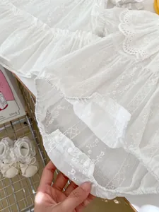 Detail eines weißen Baby-Stramplers aus Baumwolle mit Spitzenstickerei und Druckknöpfen