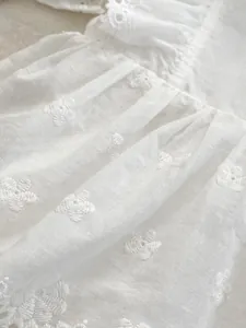 Detailed view of white cotton fabric with exquisite floral embroidery and pleats
