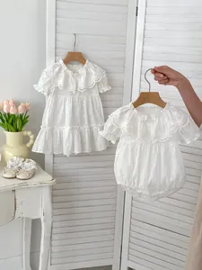 Detail von Babykleid und Body aus weißer Baumwolle mit Spitzenkragen und Holzknöpfen