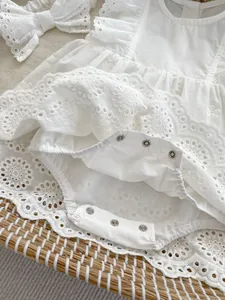 Close-up of white lace baby bodysuit with detailed snap button closure and matching headband