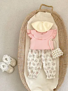 Flat lay of pink ruffled baby top with floral pants, knit beret, and pearl handbag