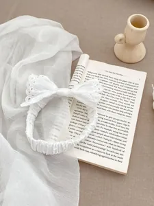 Close-up of elegant white lace bow headband with matching hair tie on neutral background