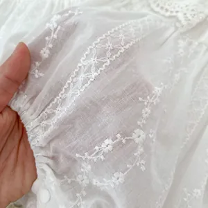 Nahaufnahme weißer Baby-Strampler mit zarter Blumenstickerei und feinen Spitzendetails